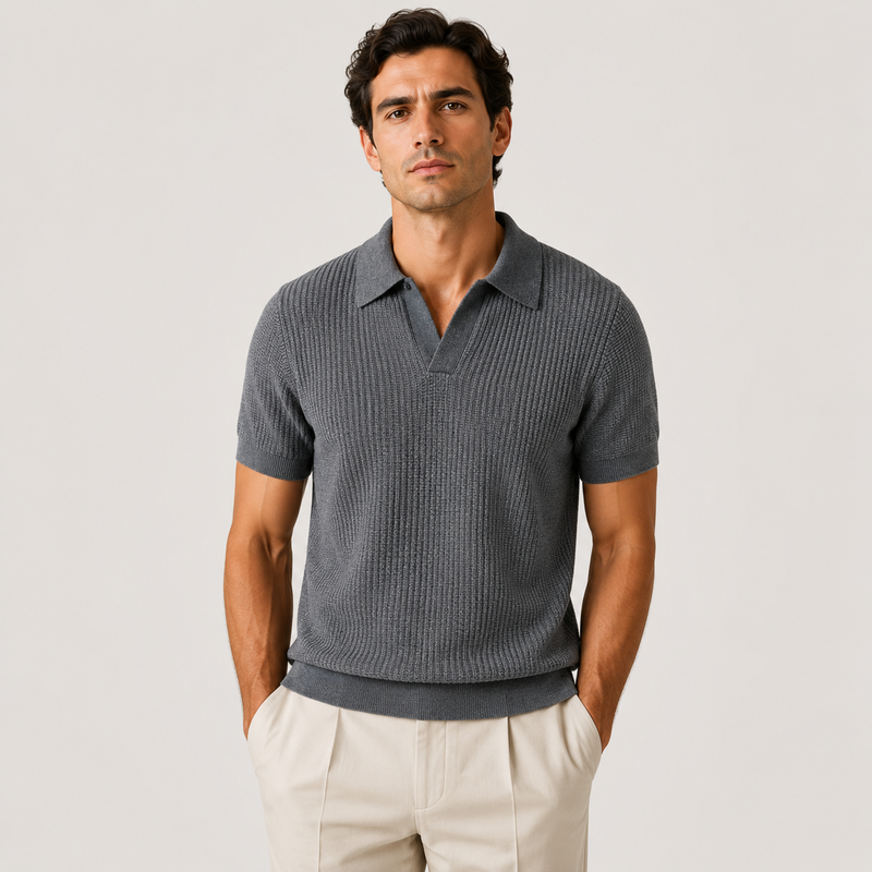 A man wearing a dark gray ribbed short-sleeve polo shirt and light beige trousers, standing against a light gray studio background.
