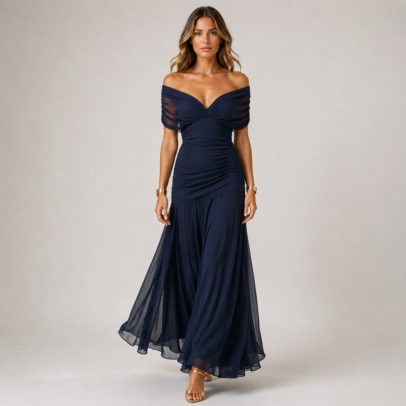 A woman modeling an off-the-shoulder navy blue maxi dress with sheer mesh sleeves and a ruched bodice, standing against a neutral light gray studio background.