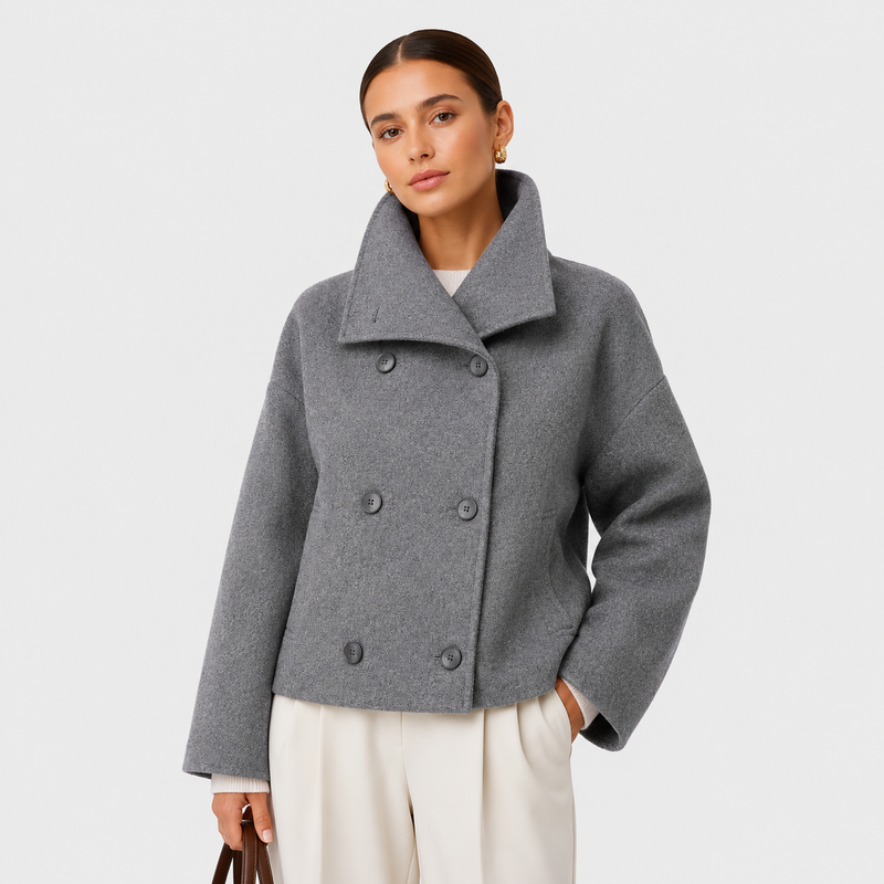 A woman modeling a gray double-breasted cropped coat with a wide collar, paired with cream trousers, against a light gray studio background.