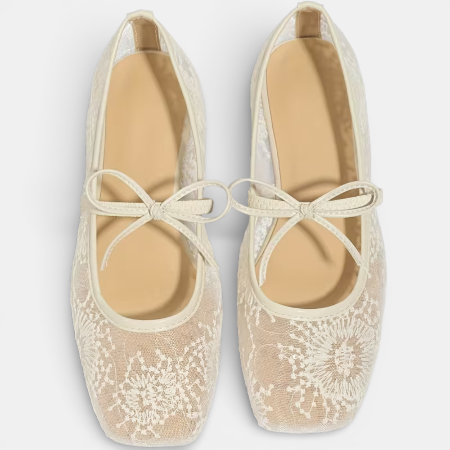 Pair of beige lace shoes with white floral patterns on a light gray background