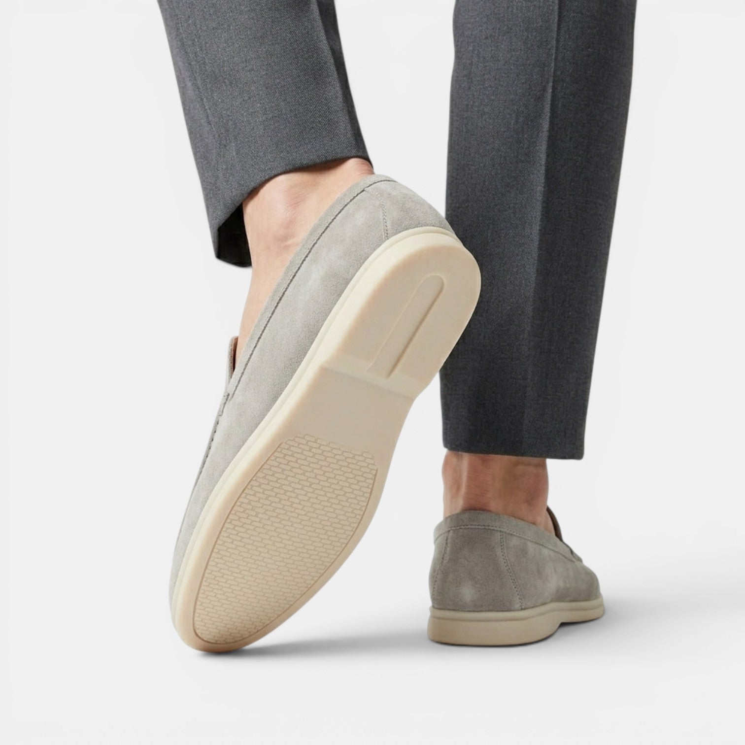 Gray suede loafers worn with gray pants on a white background