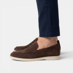 Brown suede loafers worn with navy pants on a light gray background