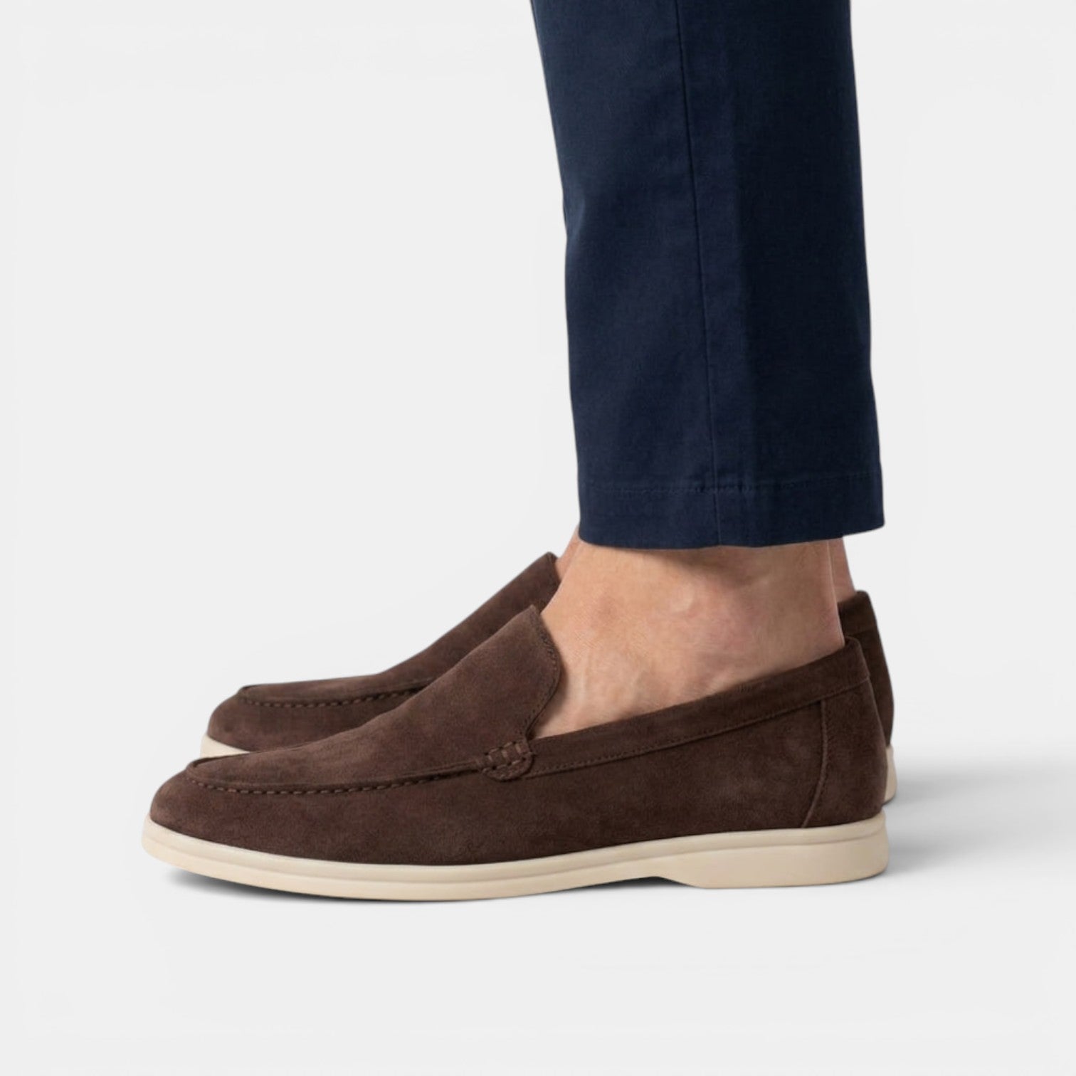 Brown suede loafers worn with navy pants on a light gray background