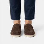 Brown suede loafers worn with navy pants on a white background