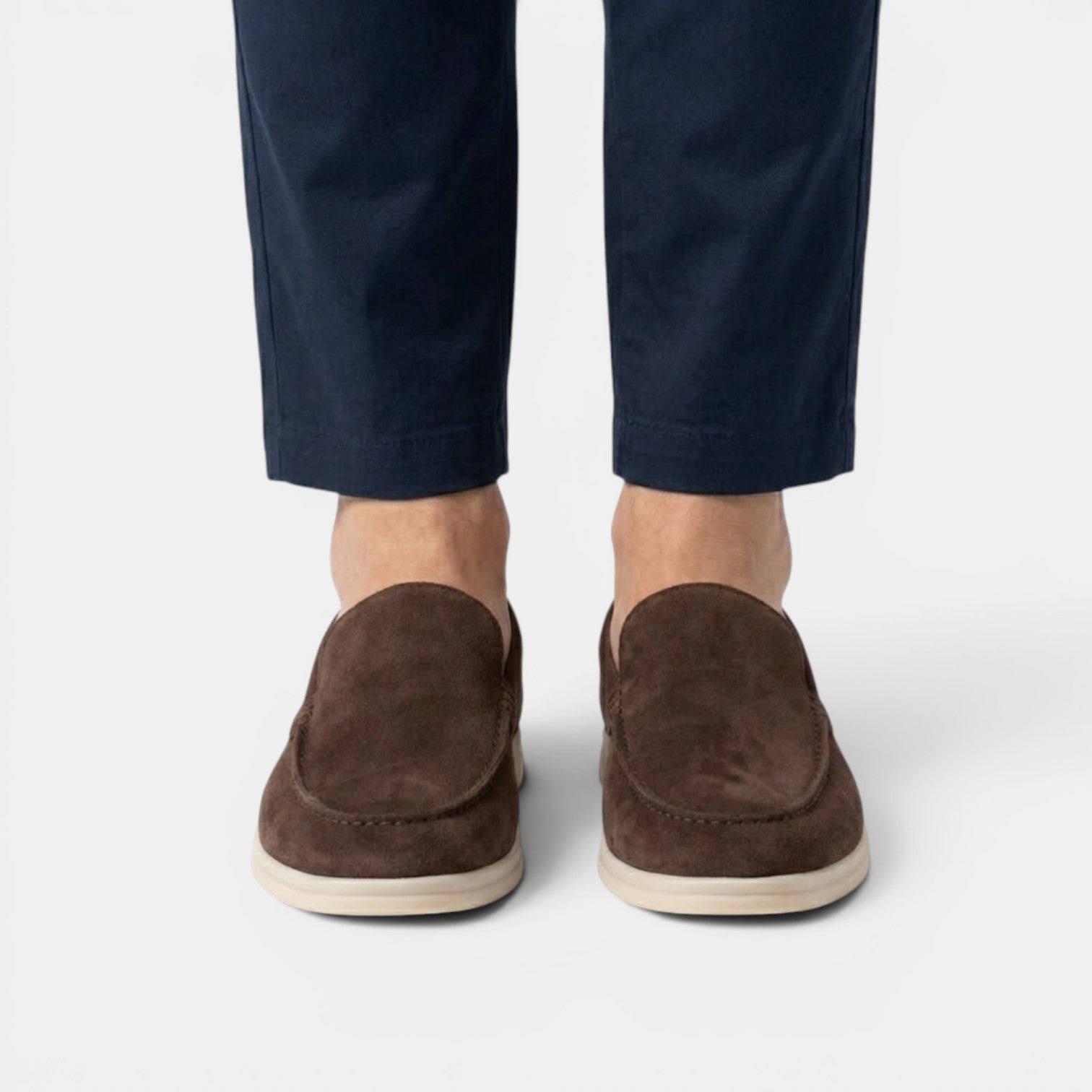 Brown suede loafers worn with navy pants on a white background