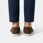 Brown suede shoes worn with navy pants on a white background