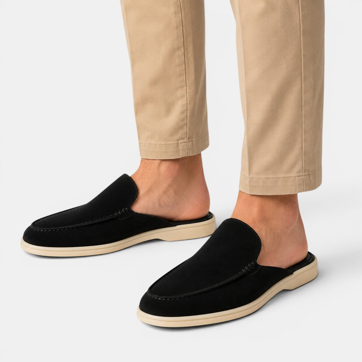 Black loafers worn with beige pants on a white background