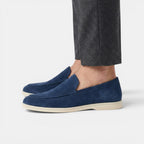 Navy loafers worn with gray pants on a white background