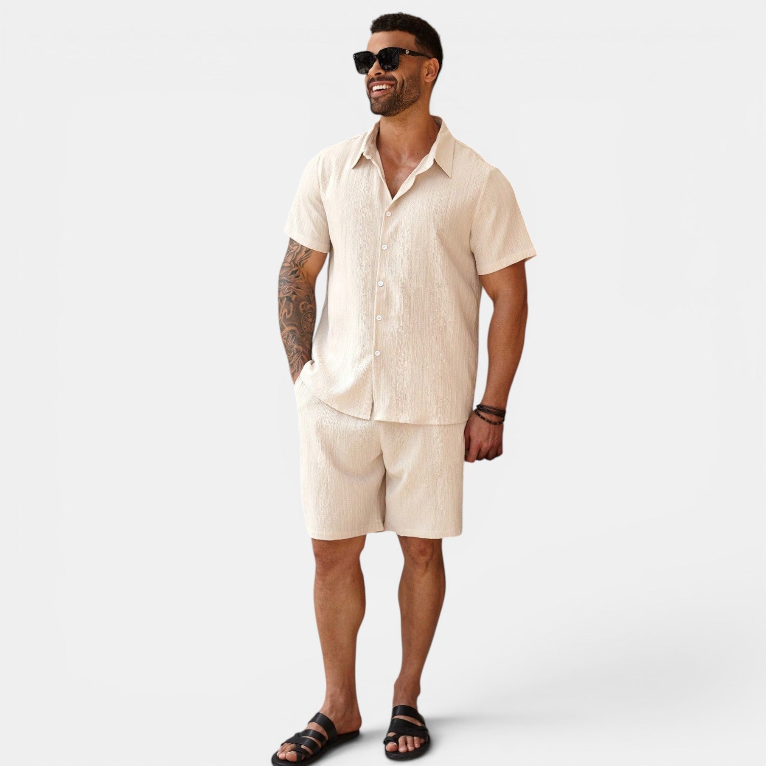 Man wearing a beige shirt and shorts set with sunglasses on a white background