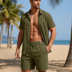 Man wearing an olive green shirt and shorts on a beach with palm trees in the background