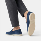 Navy loafers worn with gray pants on a white background