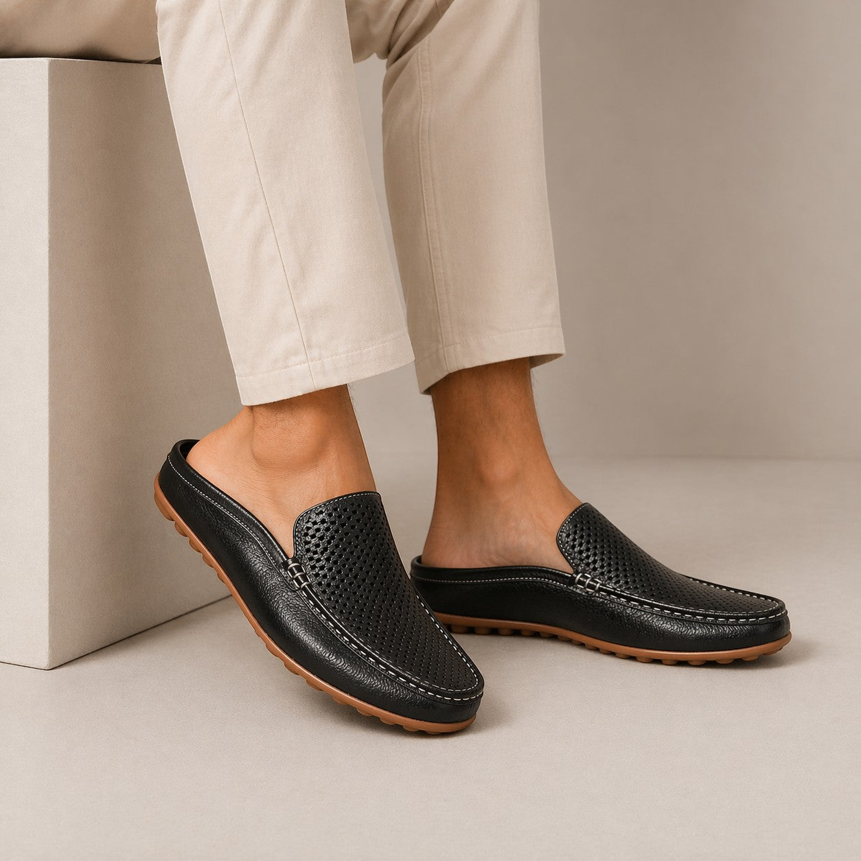 Black leather loafers worn with beige pants on a neutral background