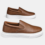 Pair of brown slip-on shoes with white soles on a light gray background