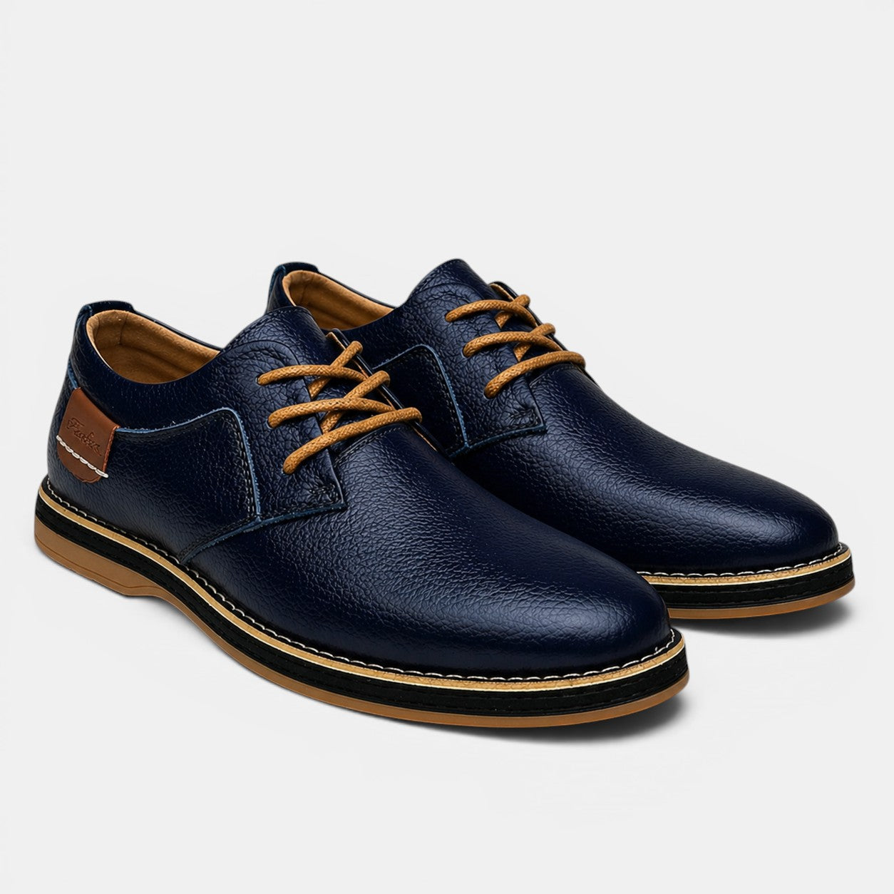 Pair of navy blue leather shoes with brown laces and sole on a light gray background