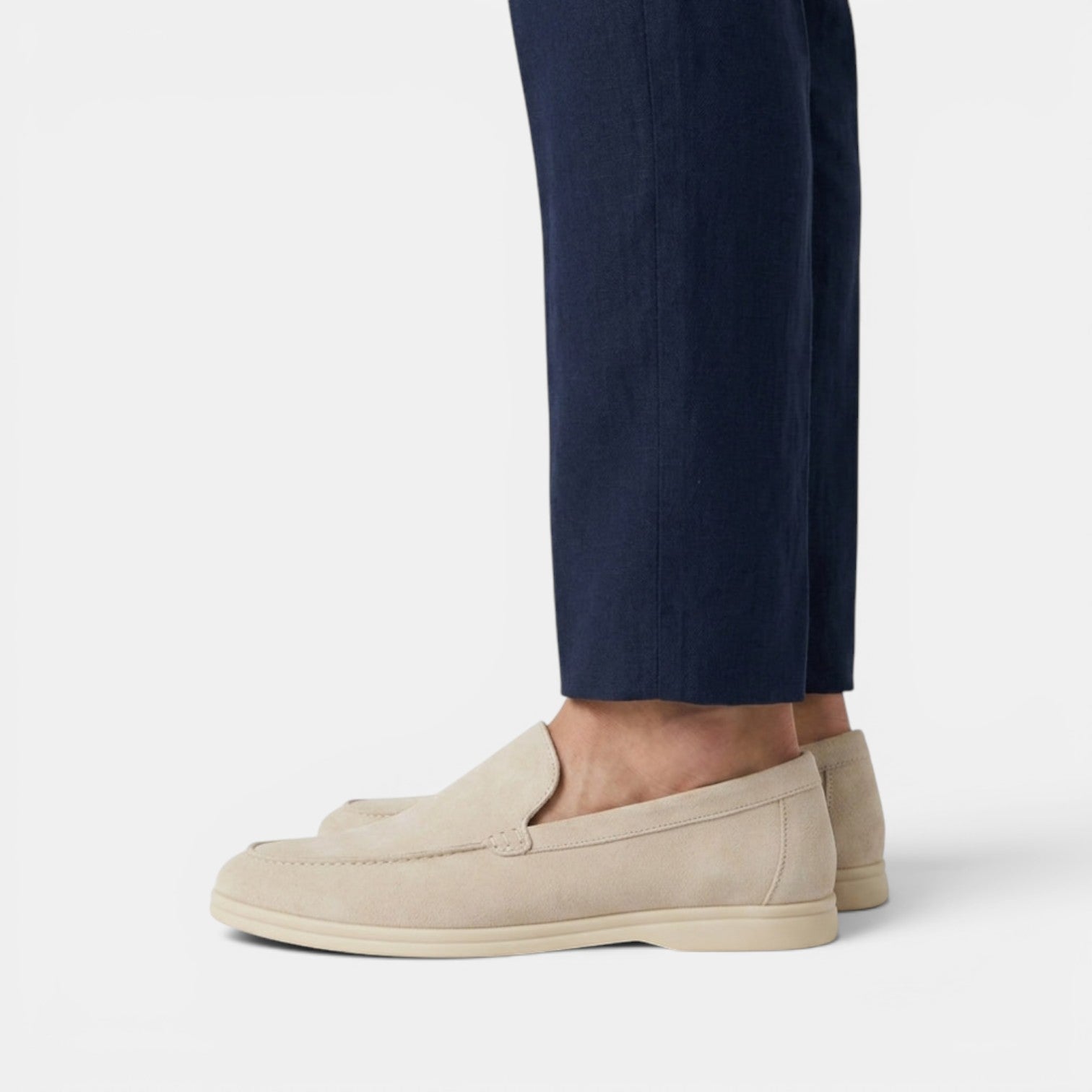 Beige loafers worn with navy pants on a light gray background