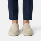 Beige loafers worn with navy pants on a light gray background