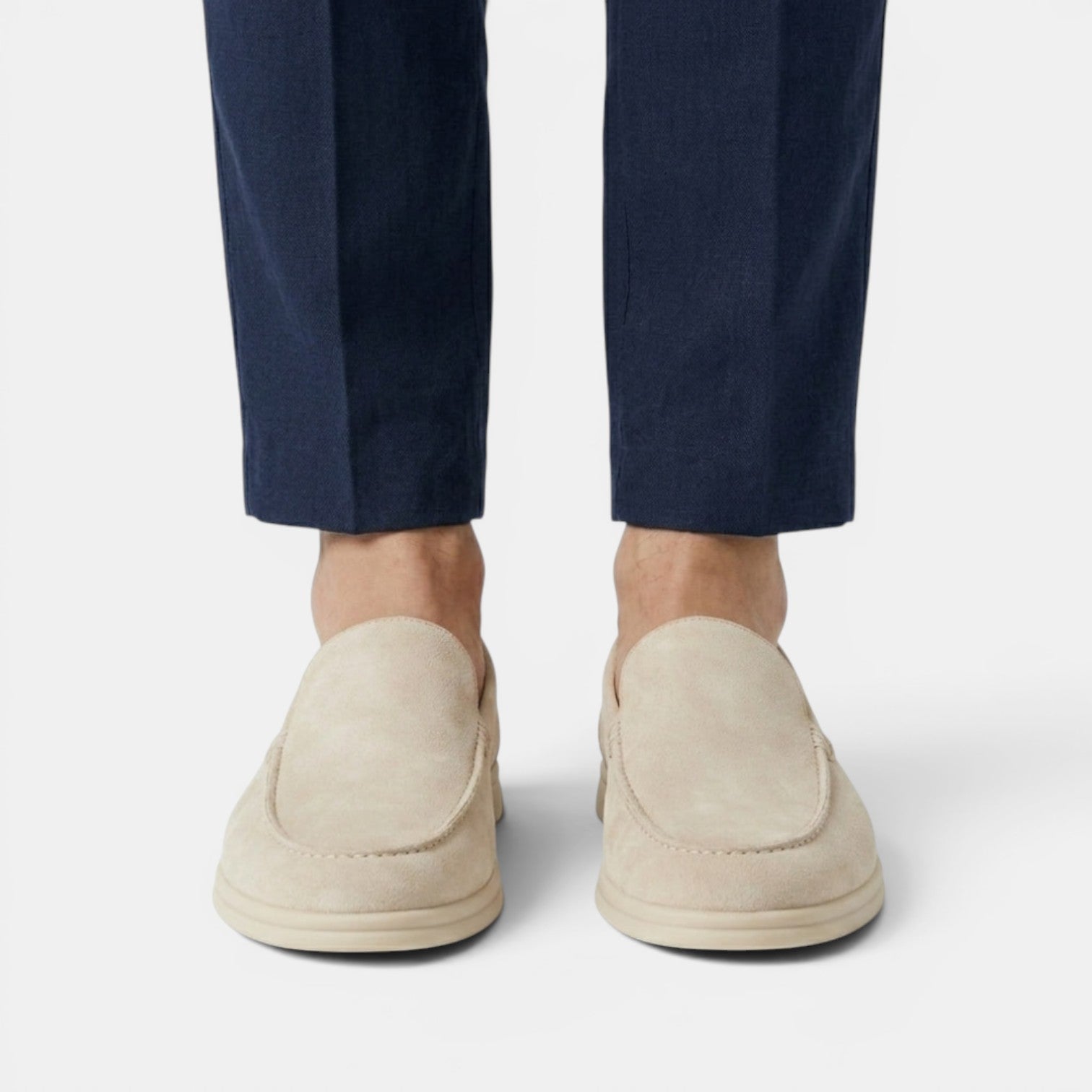 Beige loafers worn with navy pants on a light gray background