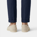 Beige slip-on shoes worn with rolled-up navy pants on a light gray background