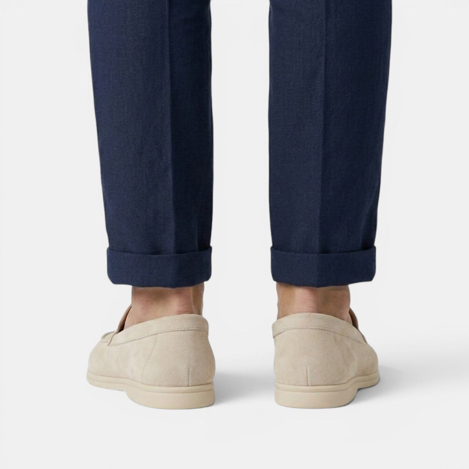 Beige slip-on shoes worn with rolled-up navy pants on a light gray background
