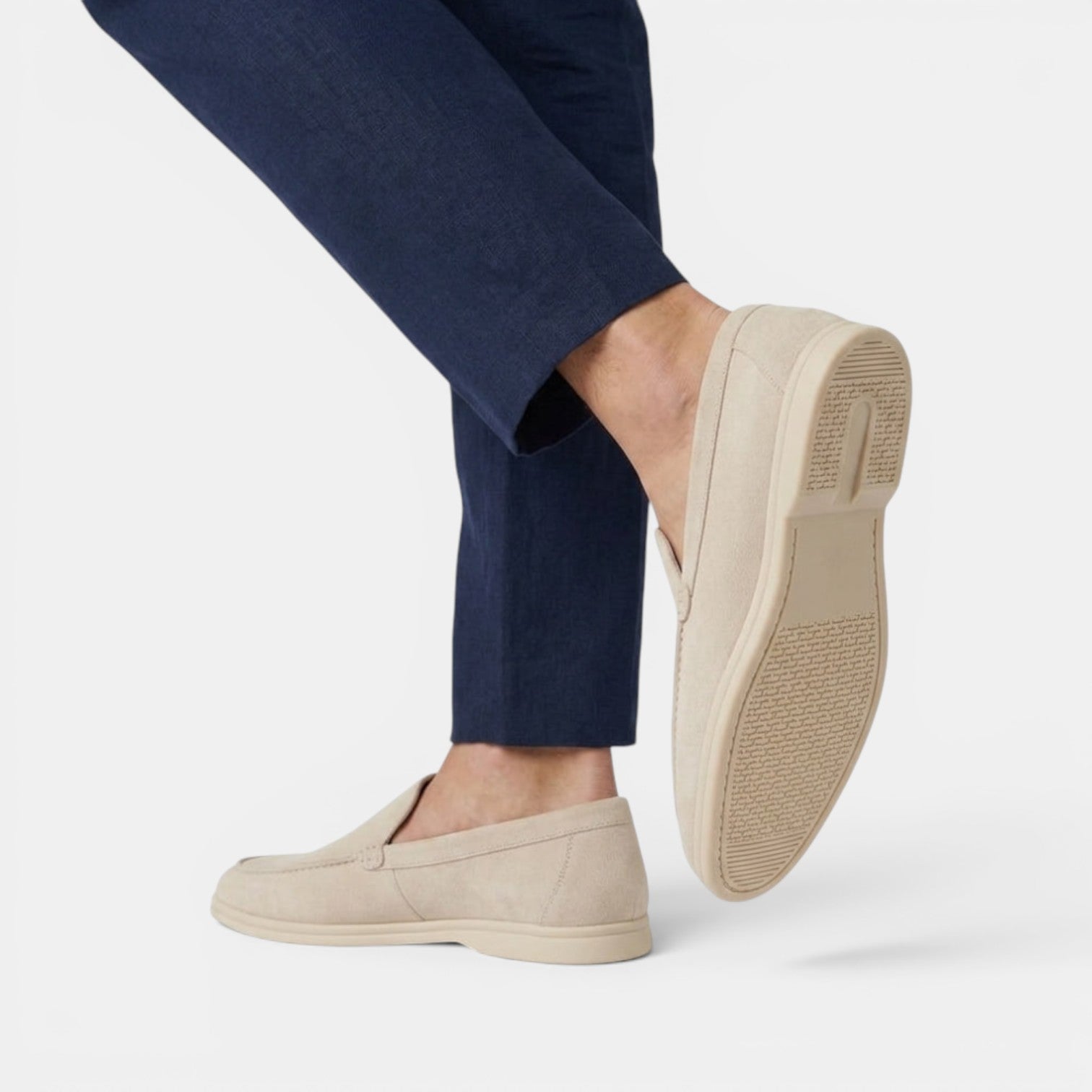 Beige slip-on shoes worn with navy pants on a white background