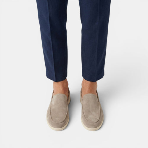 Beige loafers worn with navy pants on a white background