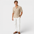 Man wearing a beige short-sleeve shirt and white pants on a light gray background