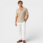 Man wearing a beige short-sleeve shirt and white pants on a light gray background