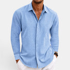 Man wearing a light blue button-up shirt with rolled-up sleeves on a white background