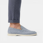 Light blue loafers worn with rolled-up dark pants on a light gray background