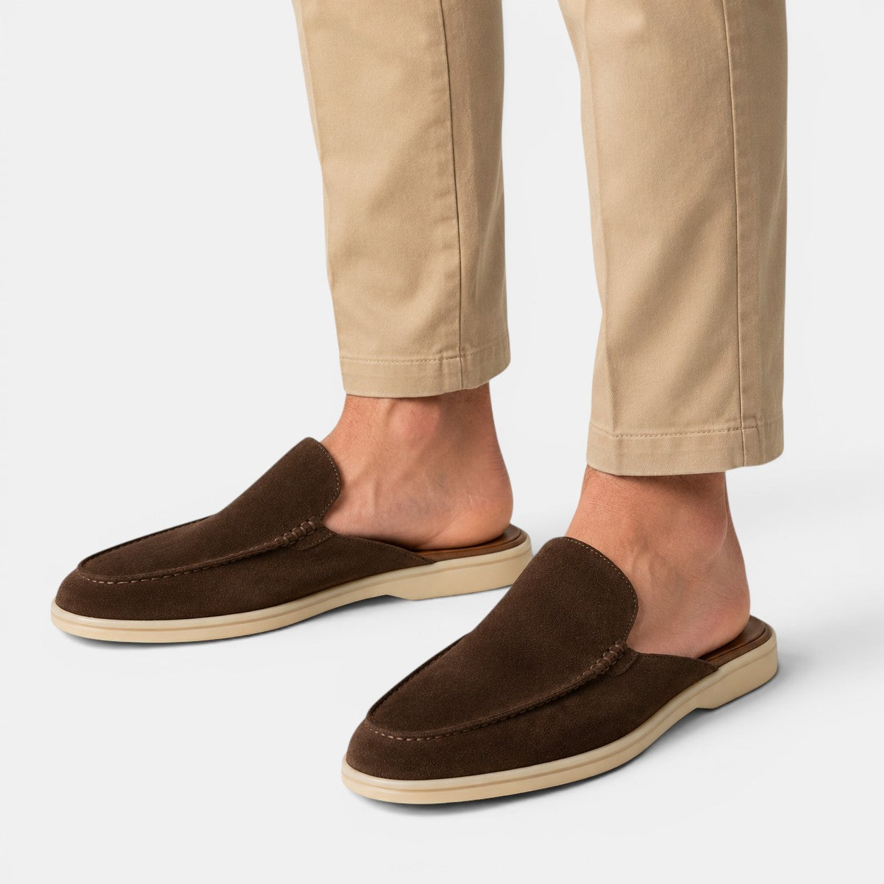 Brown loafers worn with beige pants on a light gray background
