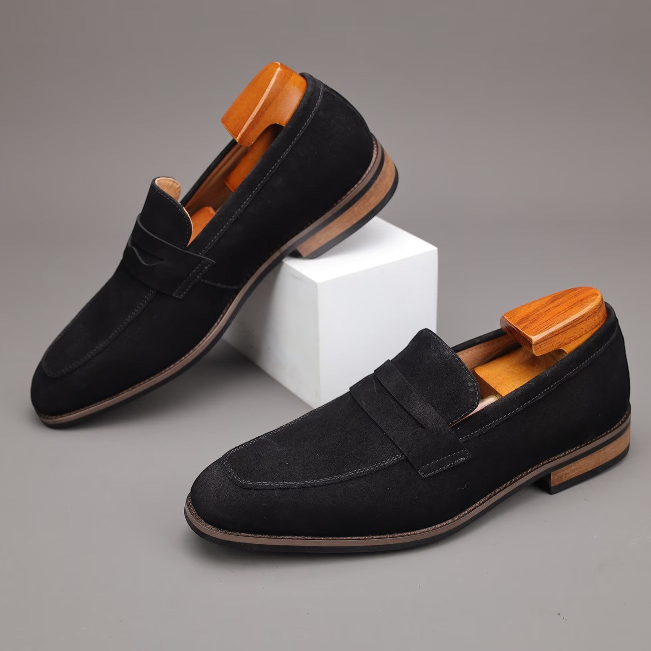 Black loafers with wooden accents on a gray background