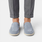 Person wearing light blue suede loafers with rolled-up gray pants on a white background