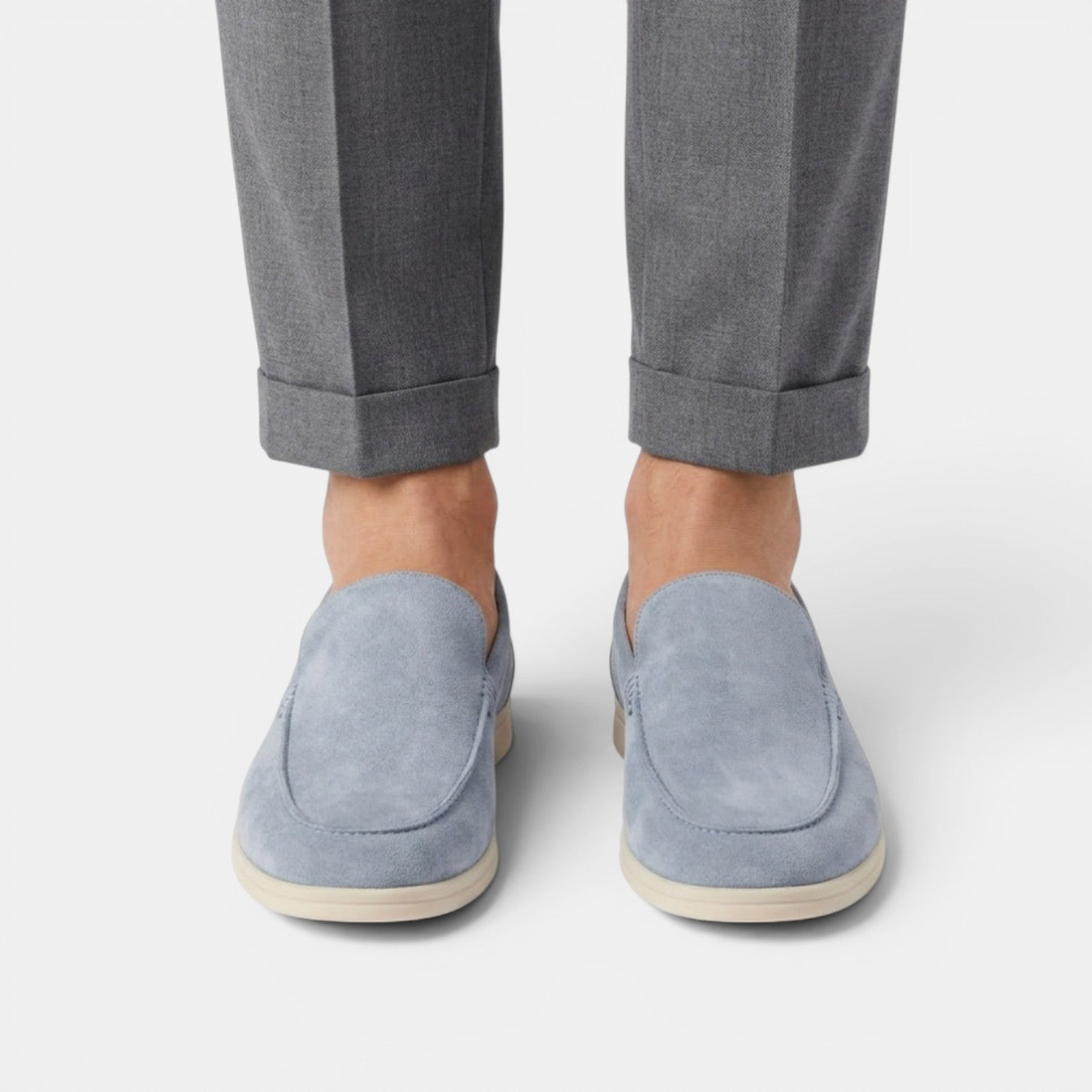 Person wearing light blue suede loafers with rolled-up gray pants on a white background