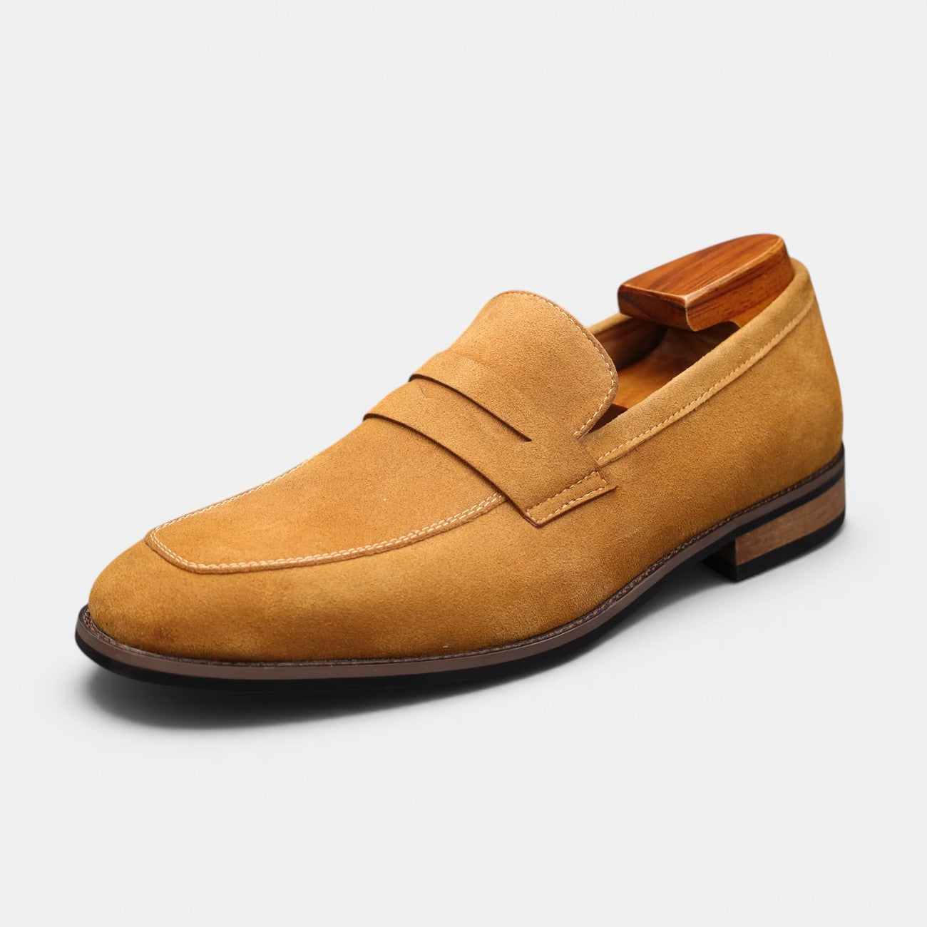Tan suede loafer with wooden buckle on a light gray background