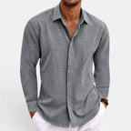 Man wearing a gray button-up shirt with rolled-up sleeves on a light background