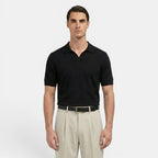 Man wearing a black polo shirt and beige pants on a white background