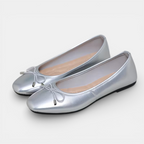 Pair of silver flat shoes with a bow on a white background