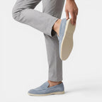 Person wearing light gray pants and blue loafers on a white background