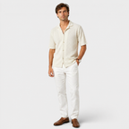 Man wearing a beige patterned shirt and white pants on a light gray background