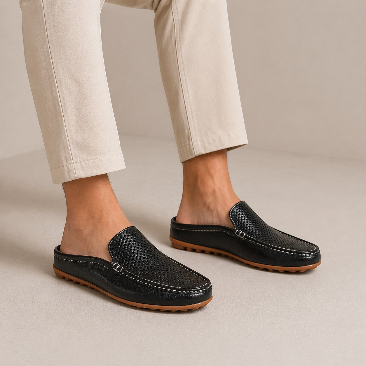 Black loafers worn with beige pants on a neutral background
