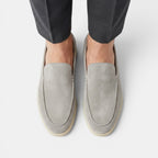 Gray loafers worn with dark pants on a white background