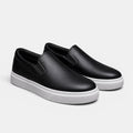 Black slip-on shoes with white soles on a light gray background