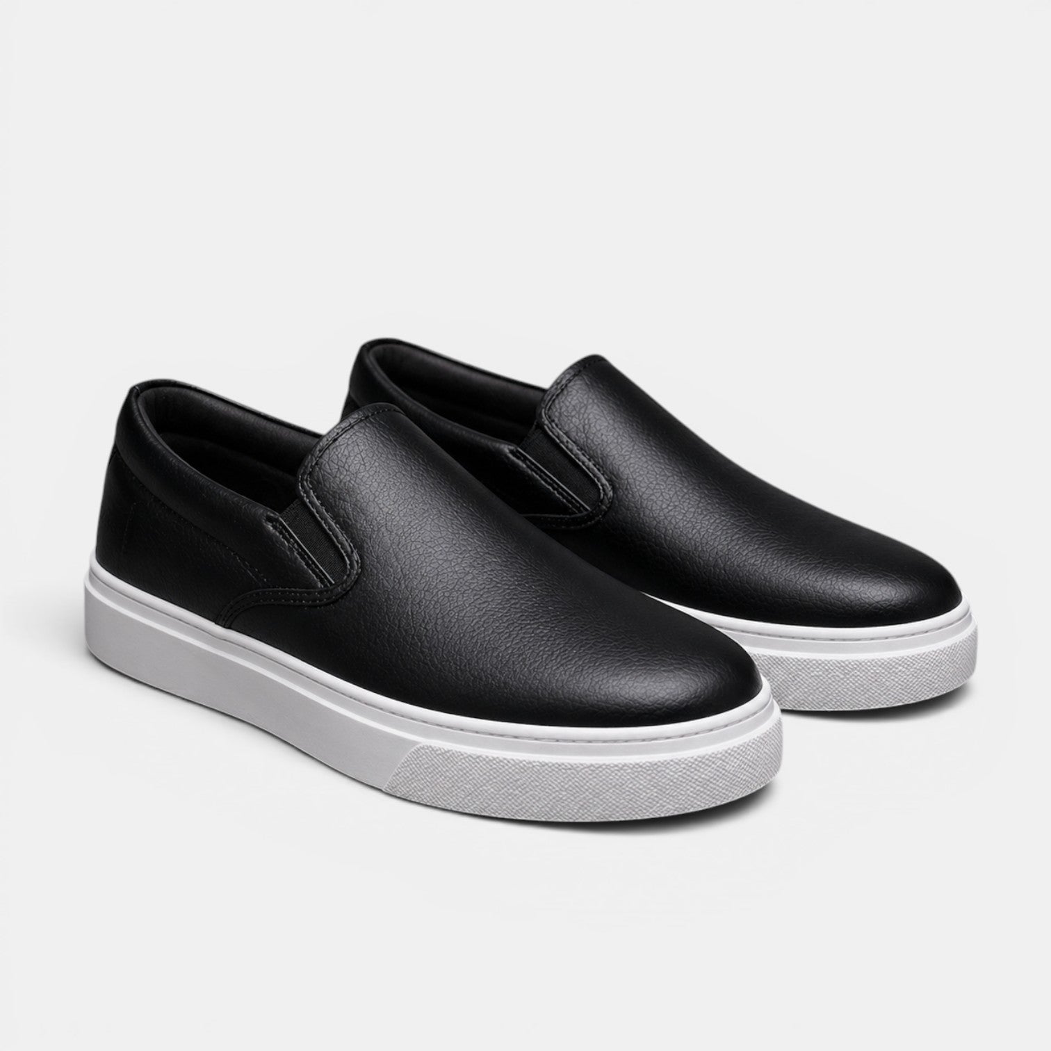 Black slip-on shoes with white soles on a light gray background