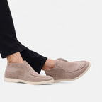 Beige loafers worn with black pants on a white background