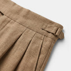 Close-up of brown pleated pants with a belt on a light gray background
