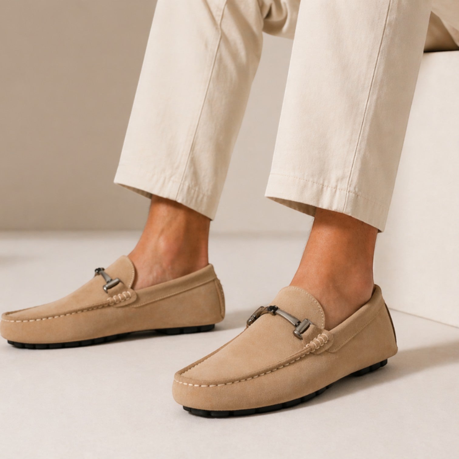 Beige loafers worn with beige pants on a neutral background