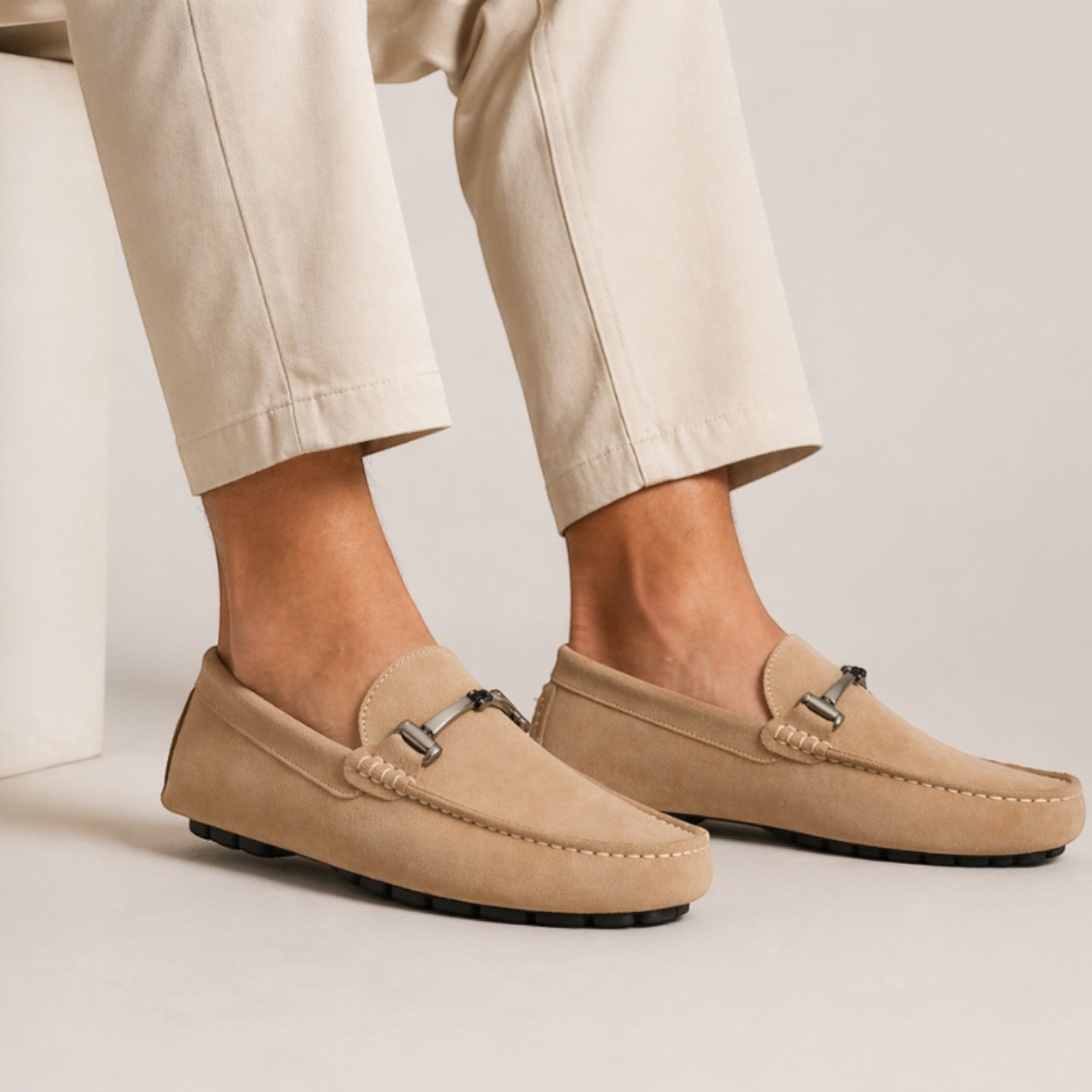 Beige loafers worn with beige pants on a neutral background