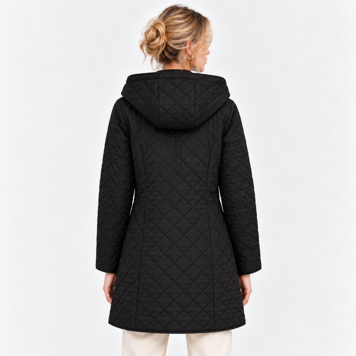 A woman viewed from the back wearing a black quilted hooded coat over cream pants, photographed against a clean light gray studio background.