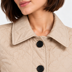 Close-up of women's beige quilted jacket with pointed collar and black buttons