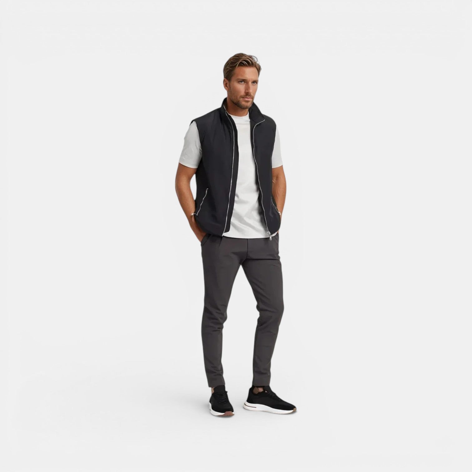Man wearing a black vest over a white shirt with gray pants on a white background